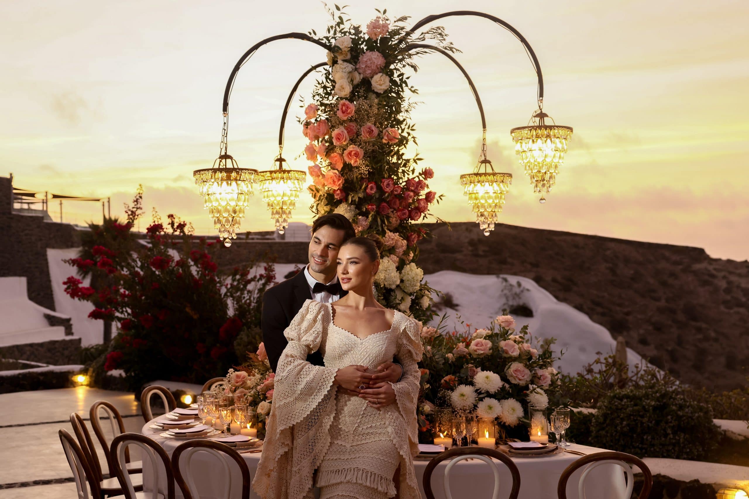 An intimate sunset elopement dinner in Santorini with a floral arch and chandeliers