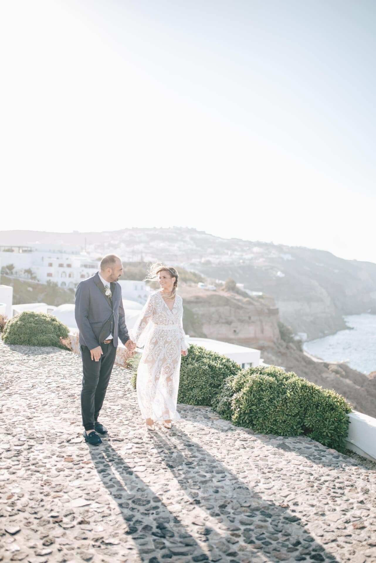 A couple walking on a whitewashed Santorini path above the sea