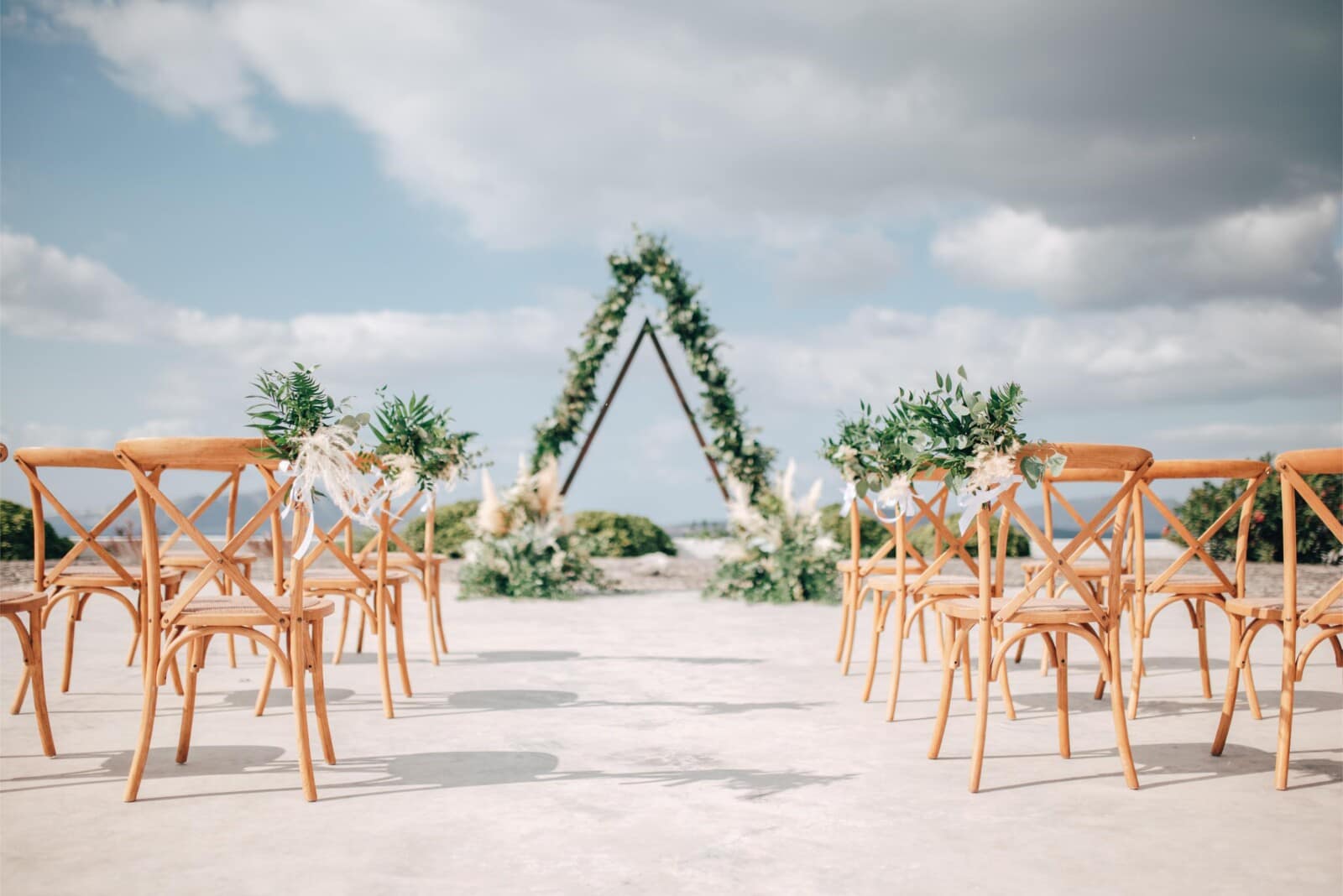 An intimate ceremony set-up with wooden chairs and a floral arch over the sea