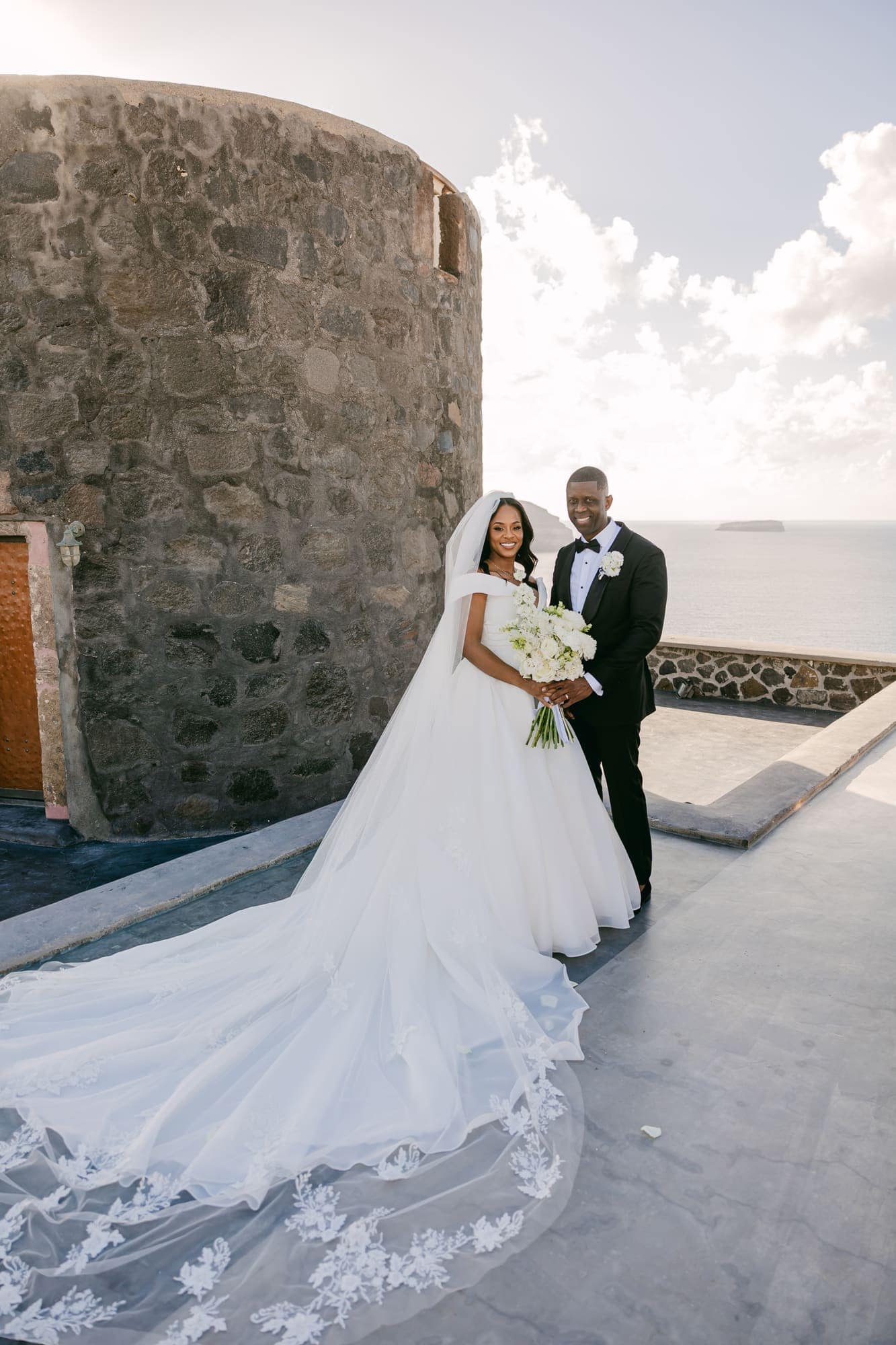 Irlon & Jailleen — portraits beneath the arch of white roses and baby's breath, Caldera terrace, Santorini