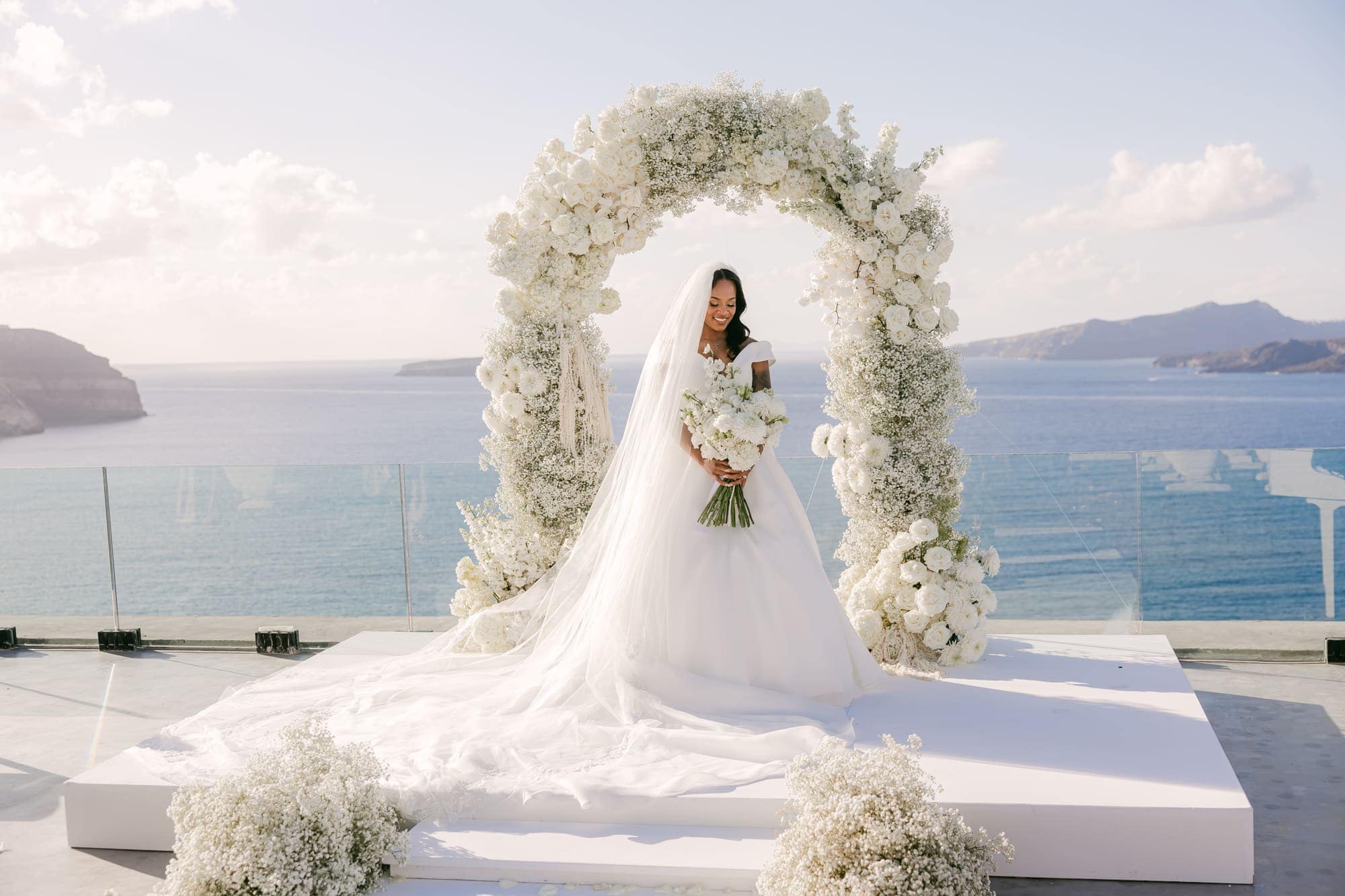 Irlon & Jailleen — portraits beneath the arch of white roses and baby's breath, Caldera terrace, Santorini