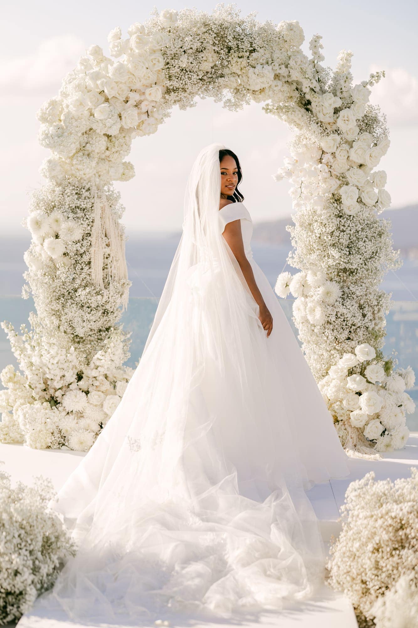 Irlon & Jailleen — portraits beneath the arch of white roses and baby's breath, Caldera terrace, Santorini