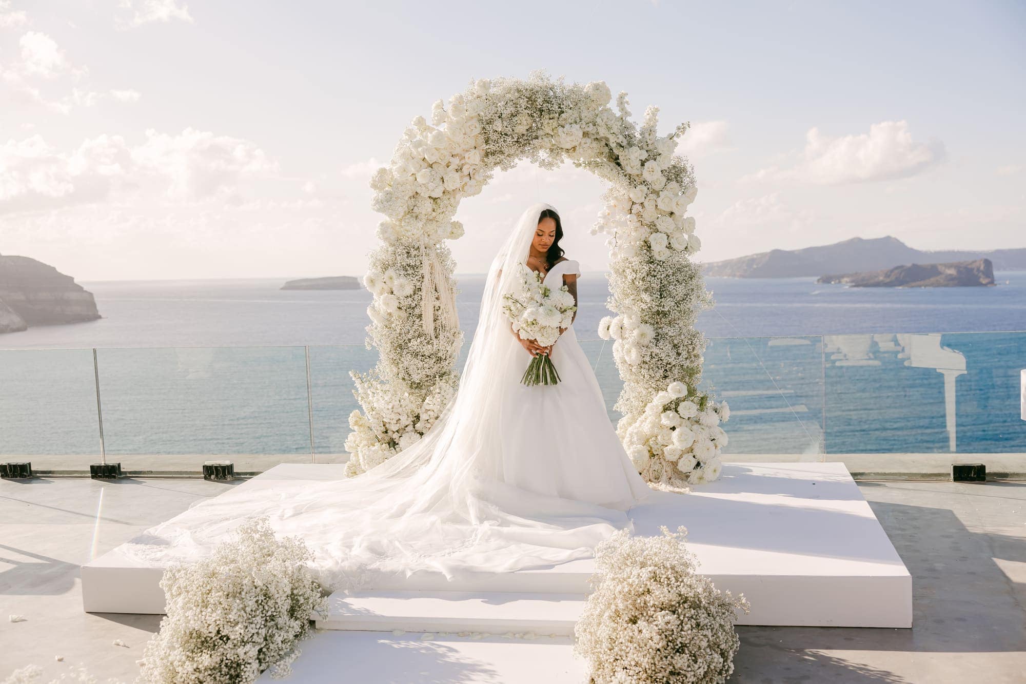 Irlon & Jailleen — portraits beneath the arch of white roses and baby's breath, Caldera terrace, Santorini