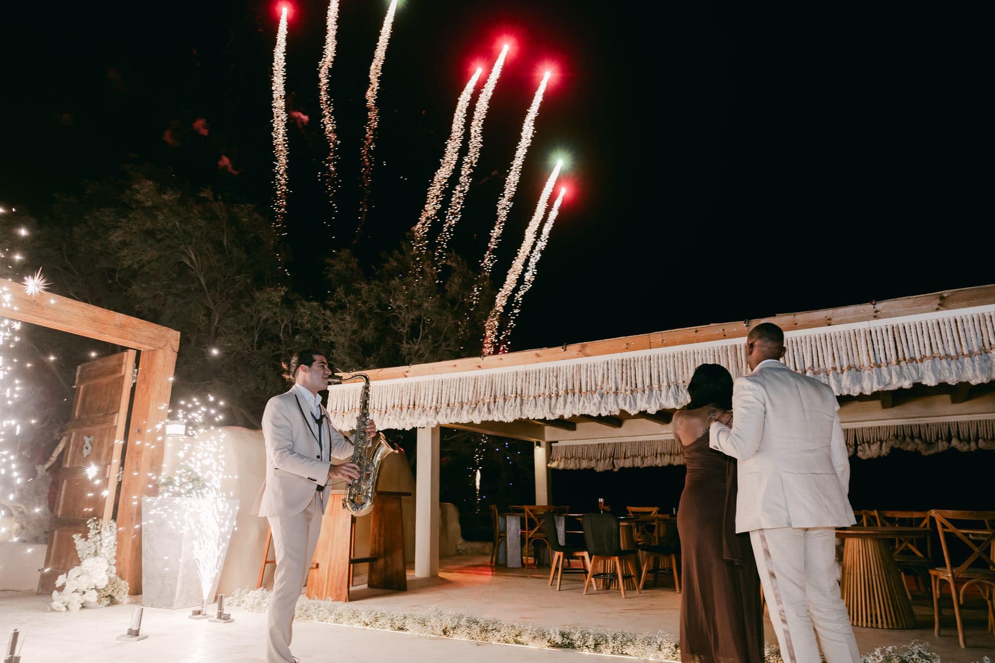 Irlon & Jailleen — fireworks and the saxophone as the party begins, Caldera terrace, Santorini