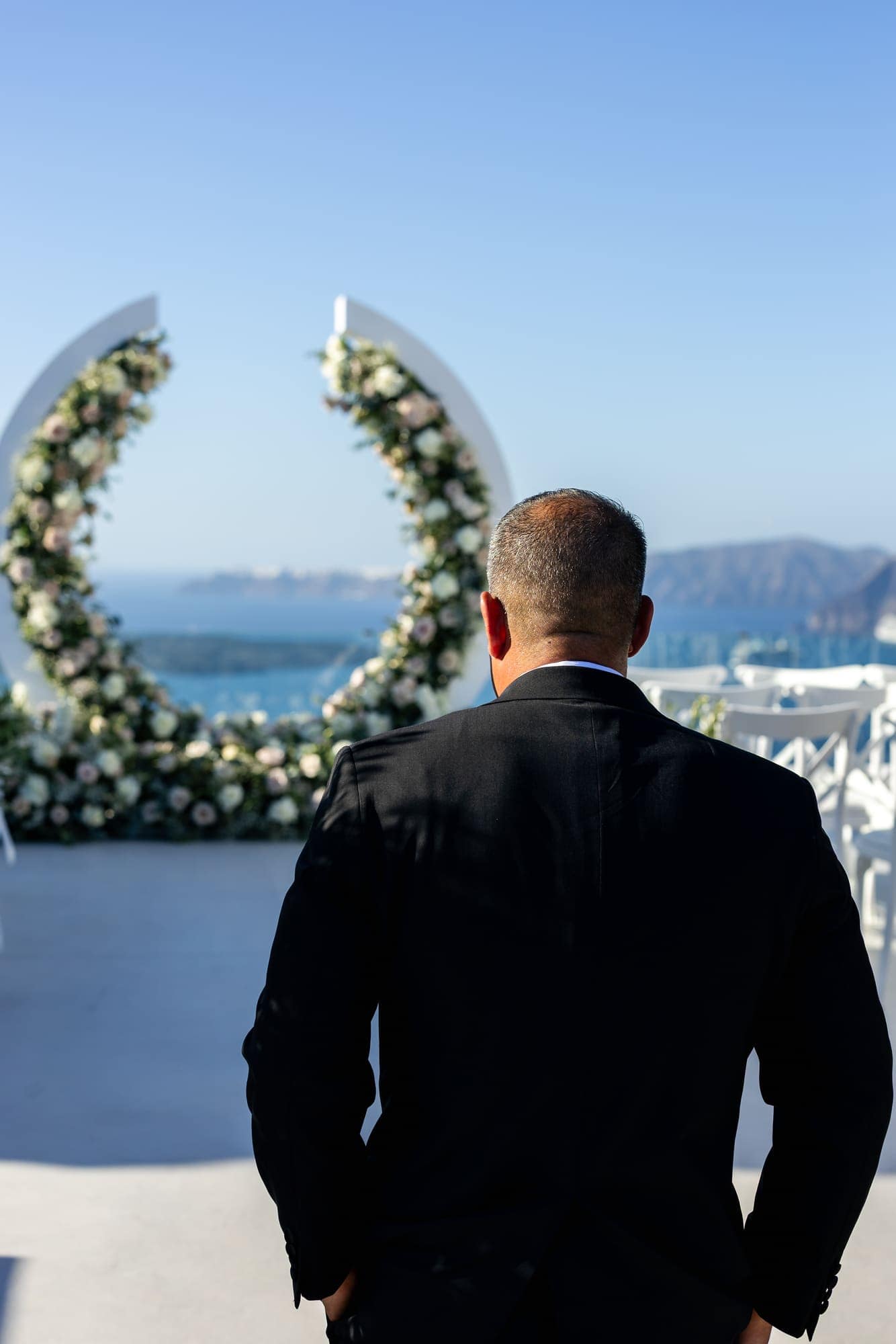 Mary & Chris — the ceremony beneath the crescent floral arch, Windmill venue on the caldera, Santorini