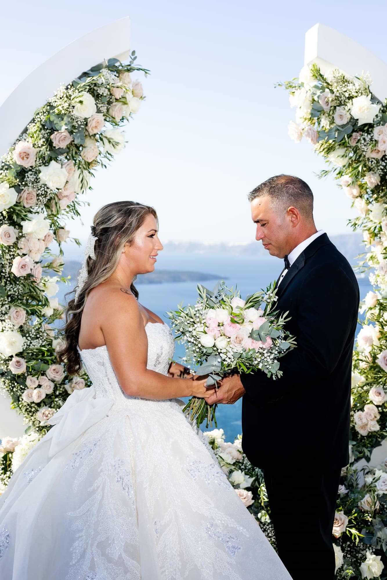 Mary & Chris — the ceremony beneath the crescent floral arch, Windmill venue on the caldera, Santorini