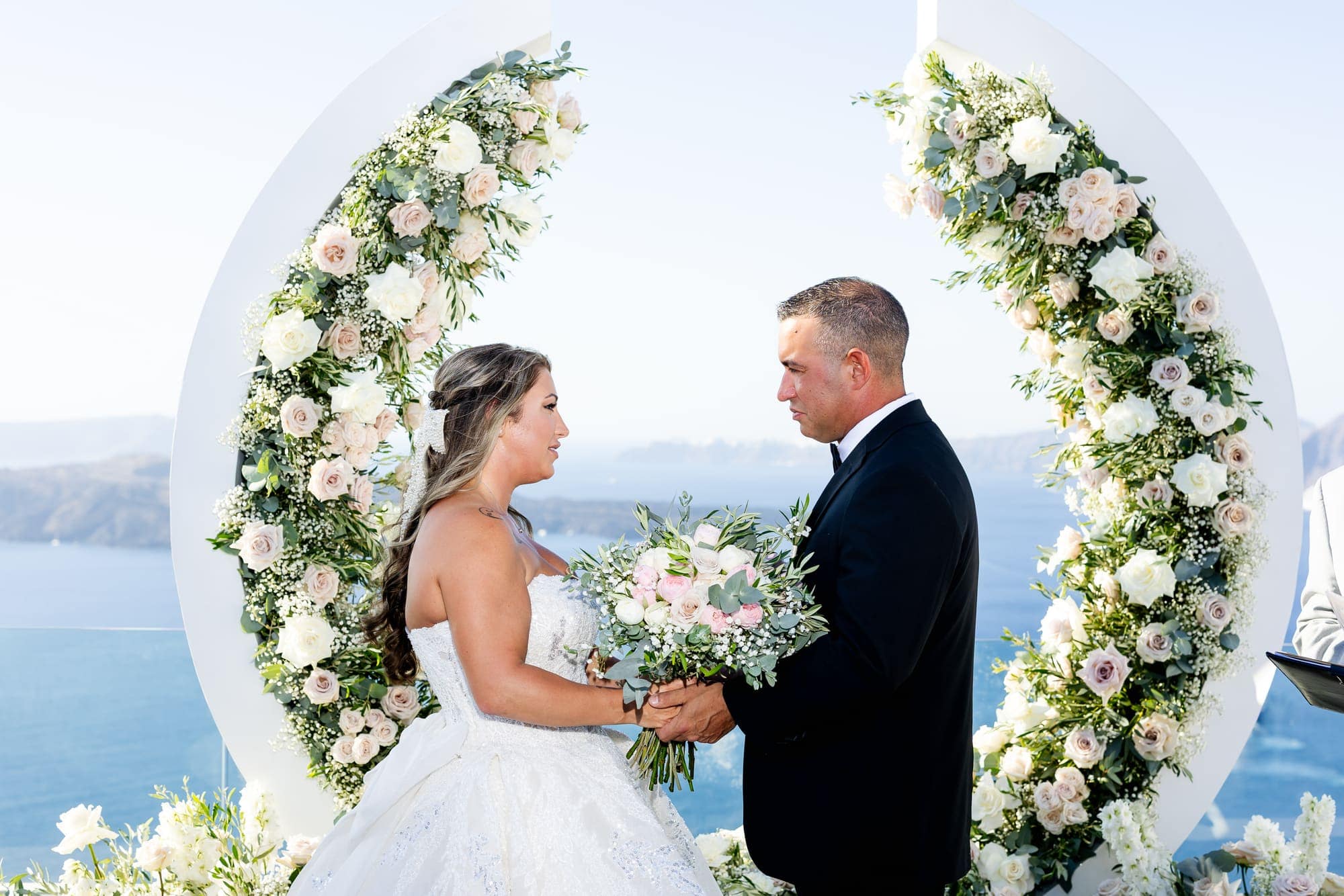 Mary & Chris — the ceremony beneath the crescent floral arch, Windmill venue on the caldera, Santorini