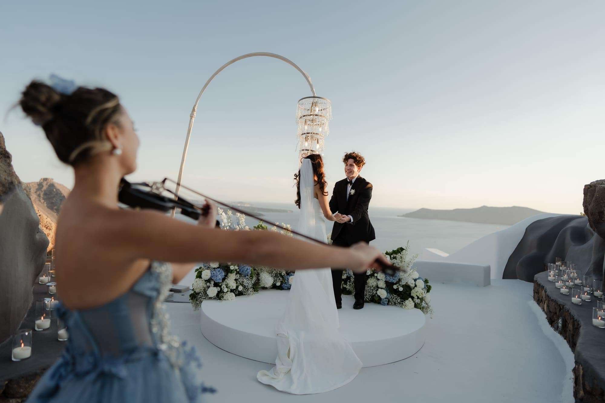 Tina & Kanon — the cake and the violin at sunset, Cliffside terrace, Santorini