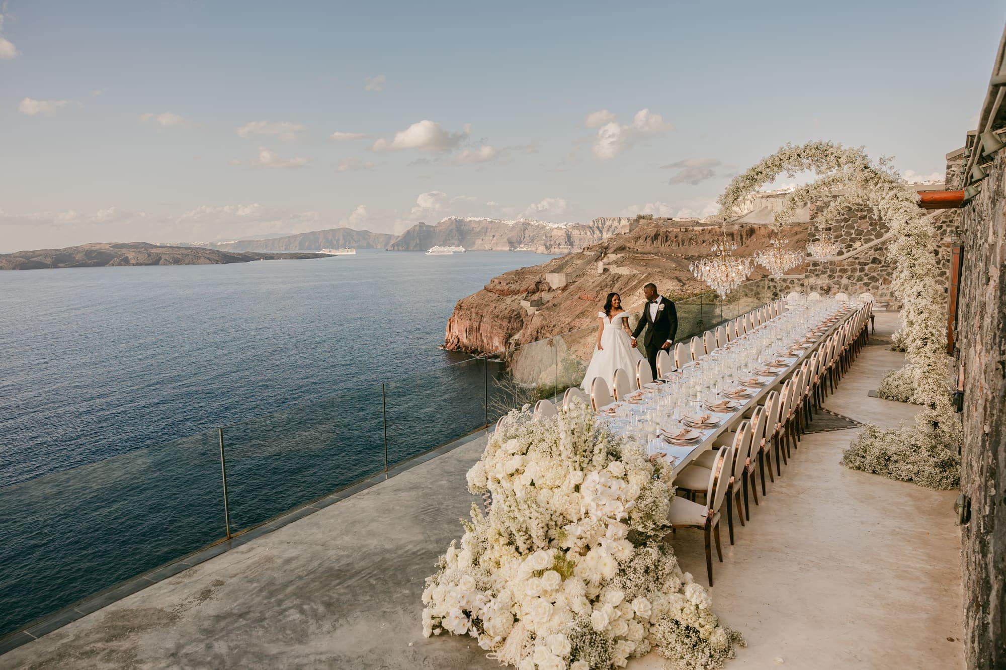 A long wedding dinner table set along the edge of the Santorini caldera